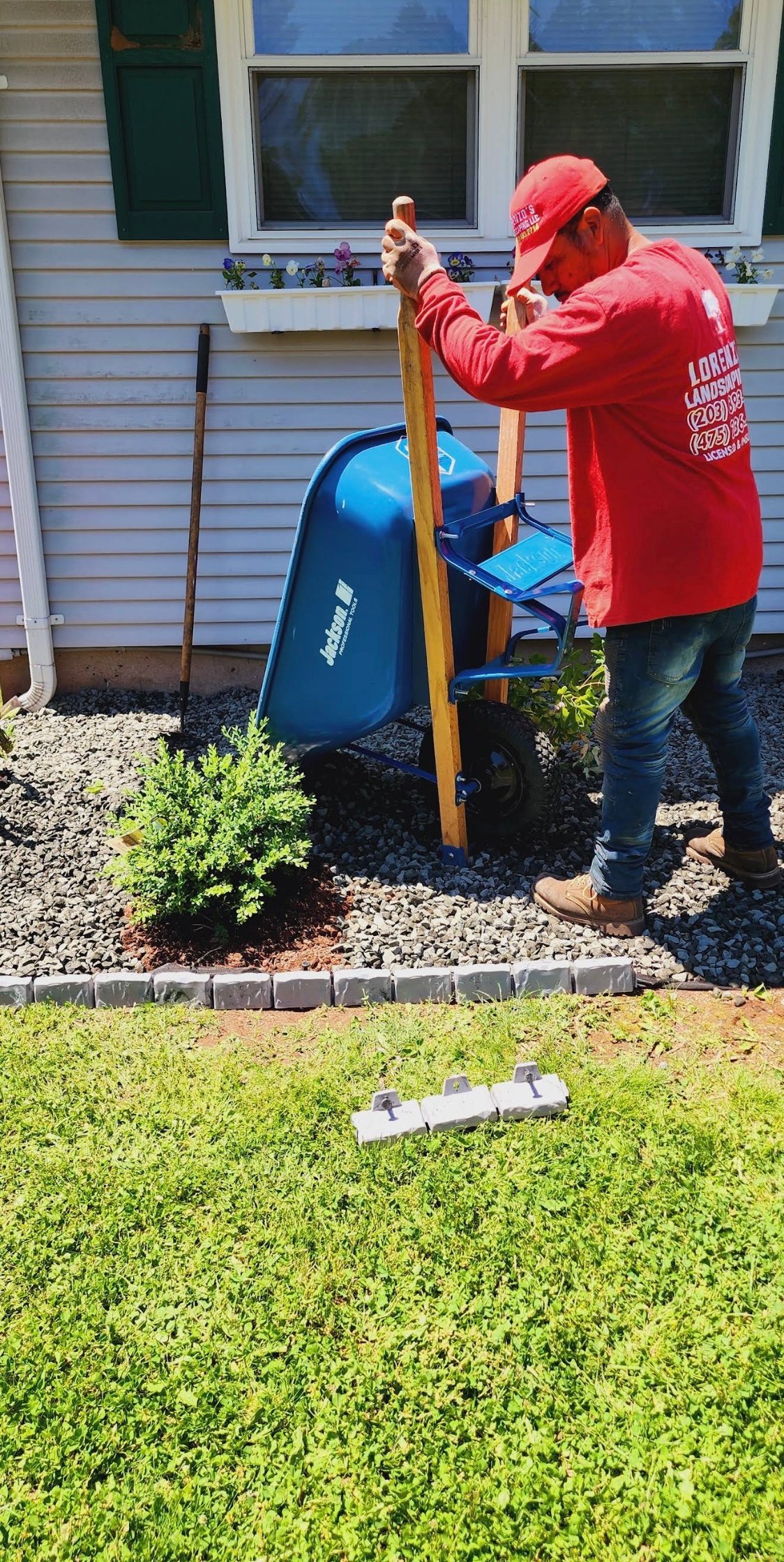 Person in red jacket operating a blue wood chipper in a residential yard next to a house