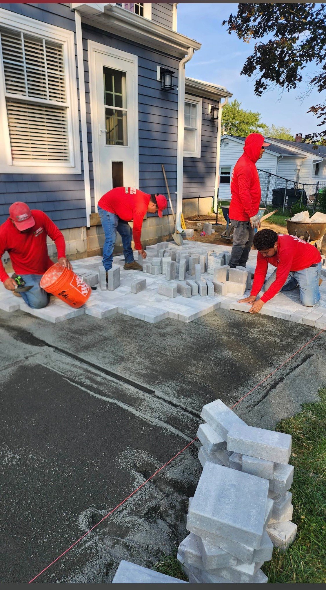 Lorenzo's crew in red shirts laying light gray concrete pavers along a residential home foundation