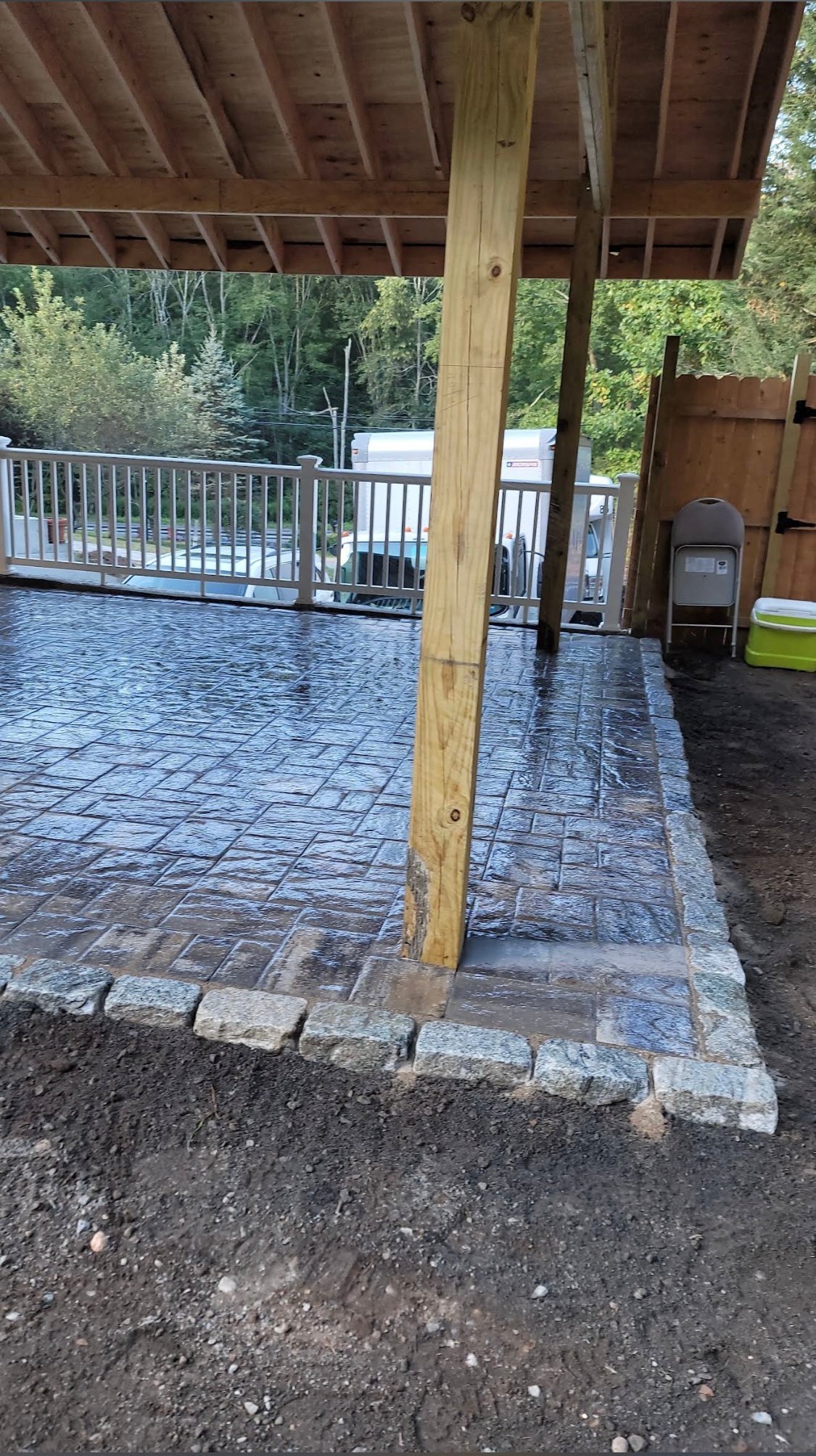 Covered patio with paver flooring, wooden support post, metal railing, and lake view in background