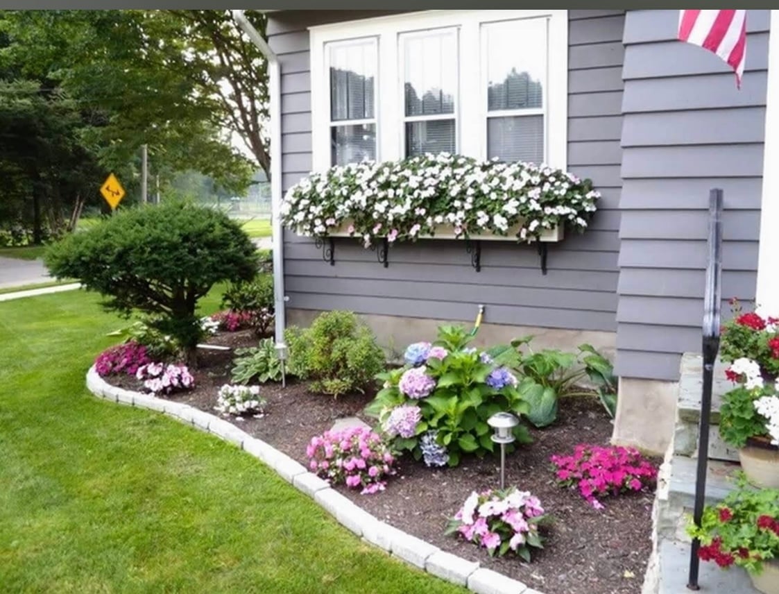Front of gray house with white window box and colorful flower garden featuring pink and purple blooms along the foundation