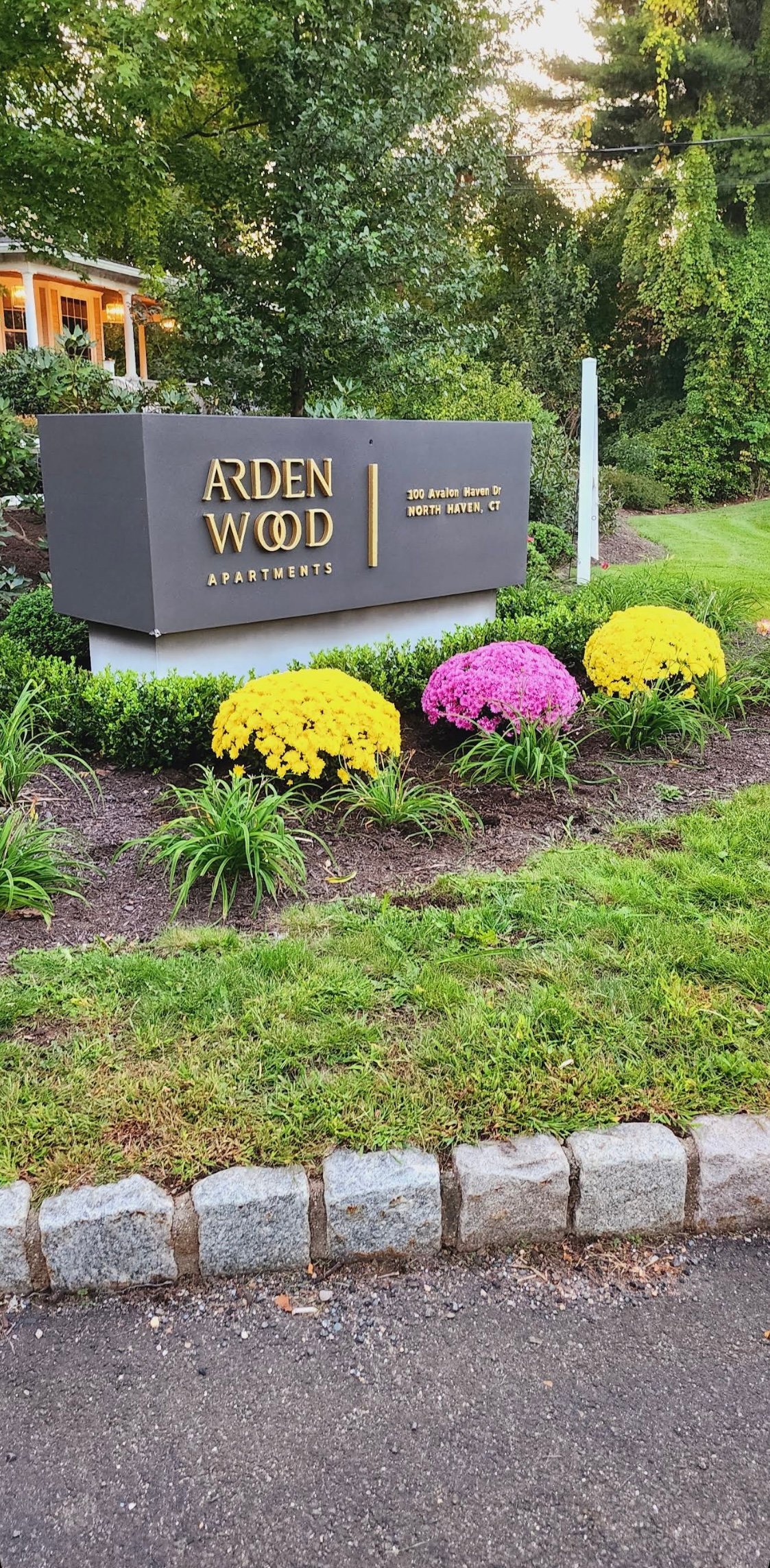 Arden Wood Apartments sign with yellow and pink chrysanthemum flowers in landscaped garden bed