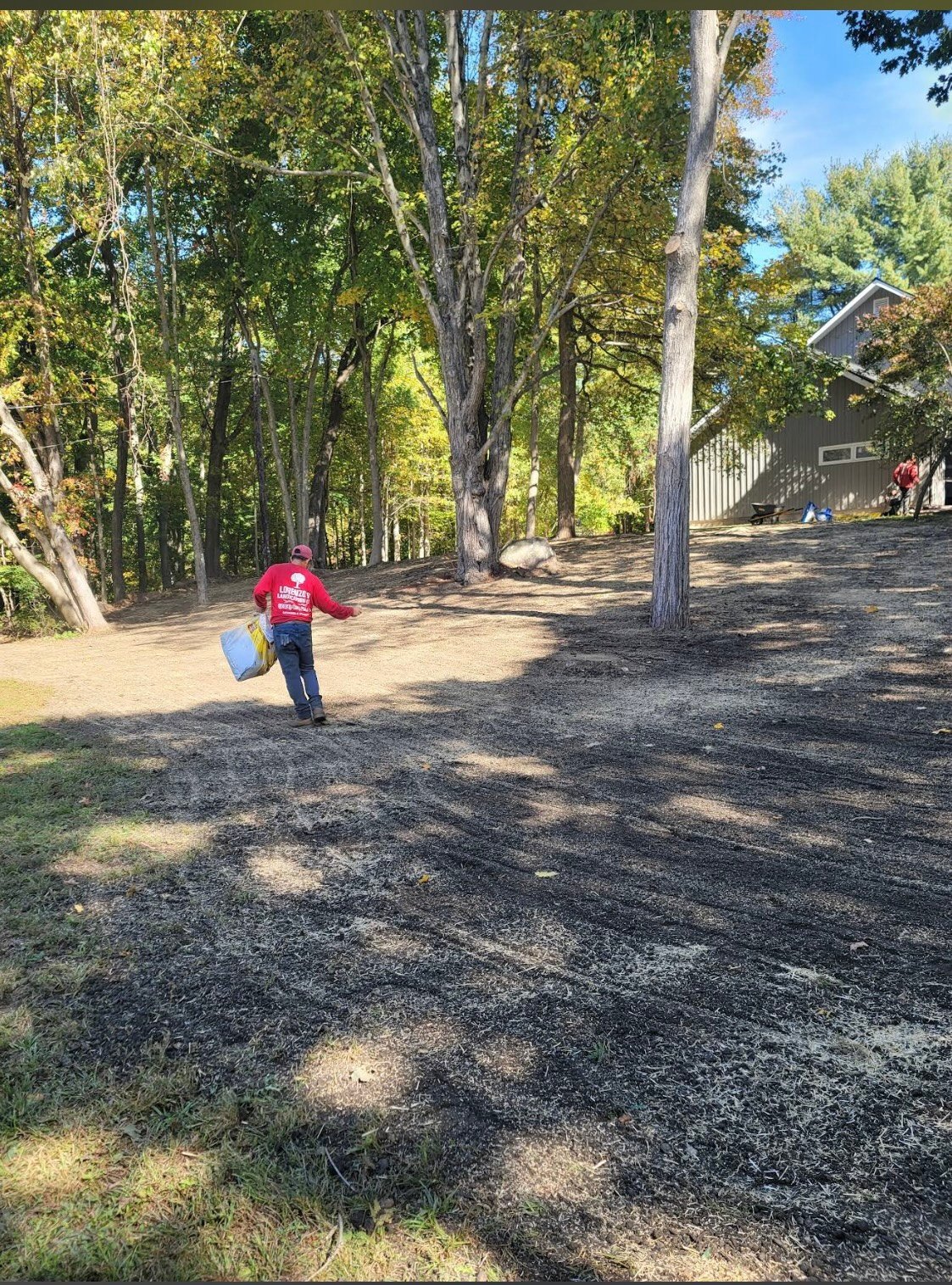 Child in red shirt running down tree-lined gravel path on sunny day with barn visible in background